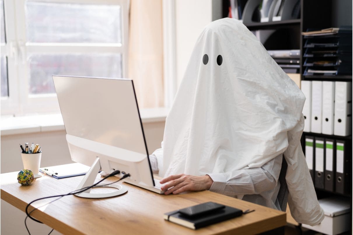 A person in a ghost costume typing on a computer.